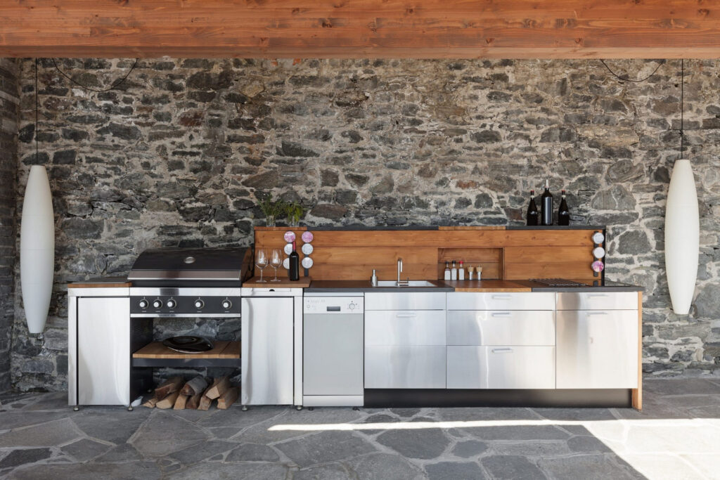 Cuisine extérieure avec barbecue, armoires en acier inoxydable et mur de pierre.